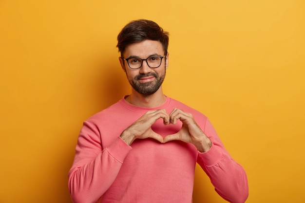 Pleased handsome man shapes heart gesture