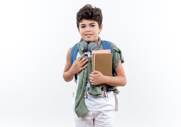 Pleased little schoolboy wearing backpack and headphones holding book 