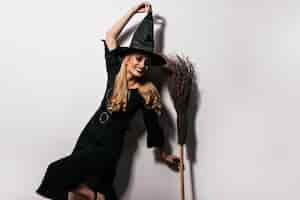 Free photo pleased long-haired witch dancing with broom. lovable female wizard having fun in halloween.