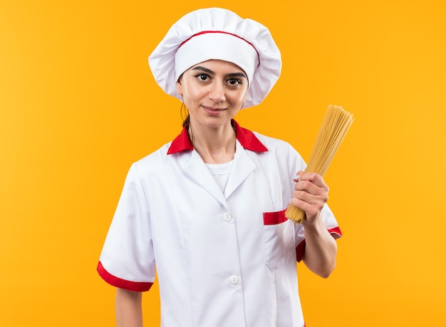 Pleased looking at side young beautiful girl in chef uniform holding spaghetti 