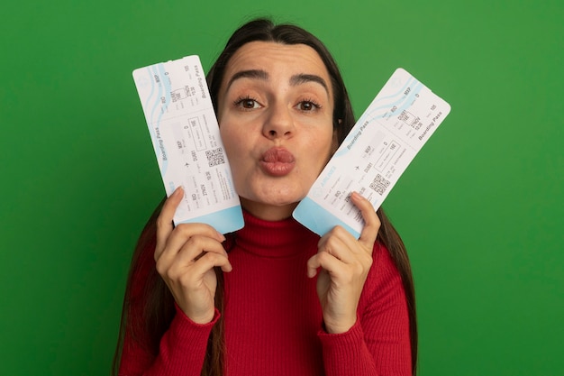 Free photo pleased pretty caucasian woman holds air tickets and doing kiss gesture on green