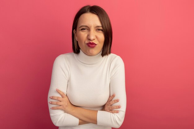 Pleased pretty woman stands with crossed arms isolated on pink wall