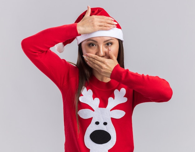 Free Photo pleased young asian girl wearing christmas hat with sweater covered forehead and mouth with hands isolated on white background