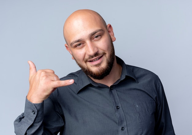 Pleased young bald call center man doing call gesture looking at camera isolated on white background