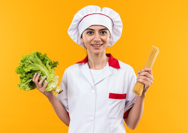 Pleased young beautiful girl in chef uniform holding salad with spaghetti 