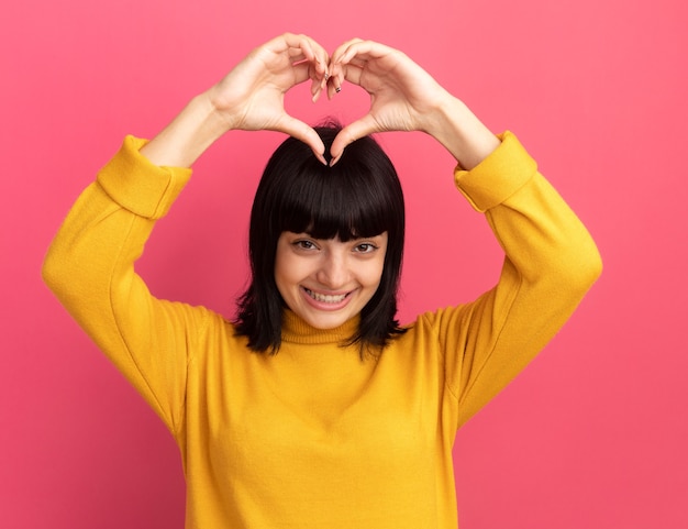 Free Photo pleased young brunette caucasian girl gestures heart sign over head