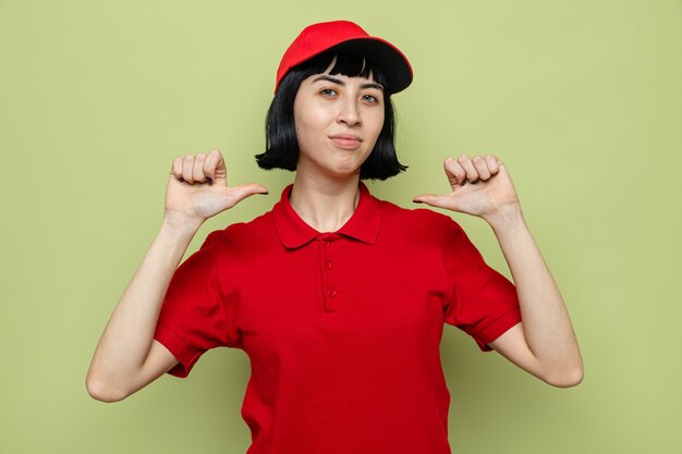 Pleased young caucasian delivery woman pointing at herself 