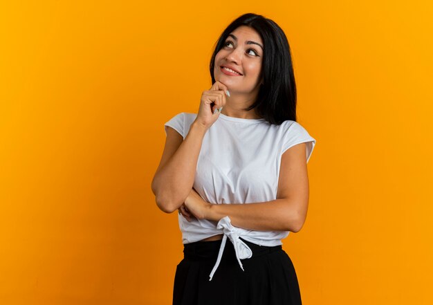 Pleased young caucasian girl puts hand on chin looking at side 