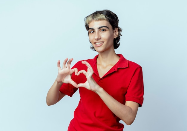 Pleased young caucasian girl with pixie haircut doing heart sign isolated on white background with copy space