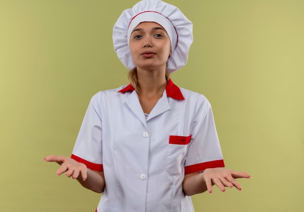 Free photo pleased young cook female wearing chef uniform speads hands on isolated green wall