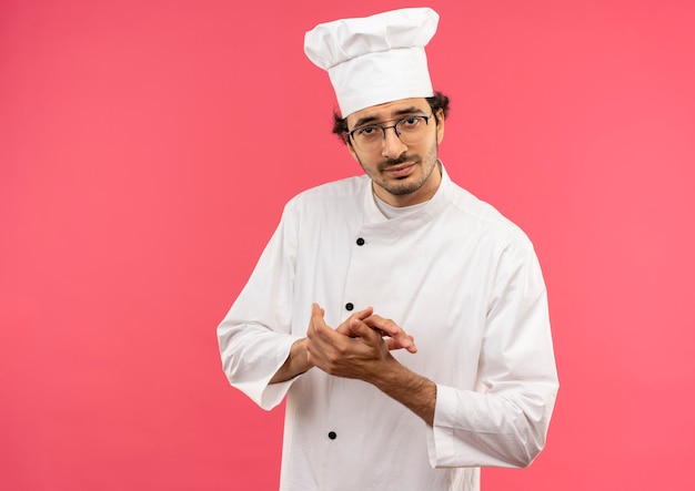 pleased young male cook wearing chef uniform and glasses holding hands together 