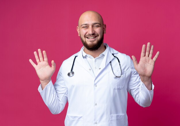 Pleased young male doctor wearing medical robe and stethoscope holding hands