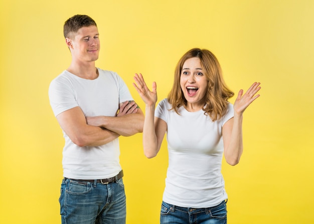 Pleased young man standing near the surprised girlfriend against yellow backdrop