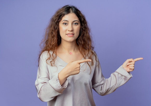 Pleased young pretty girl points at side isolated on blue wall with copy space