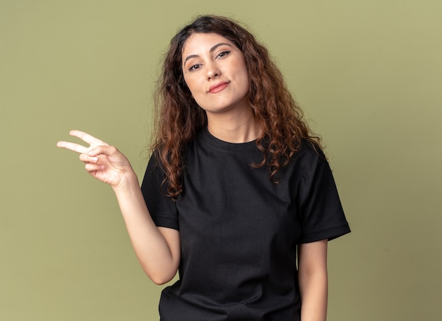 Free photo pleased young pretty woman looking at front doing peace sign isolated on olive green wall