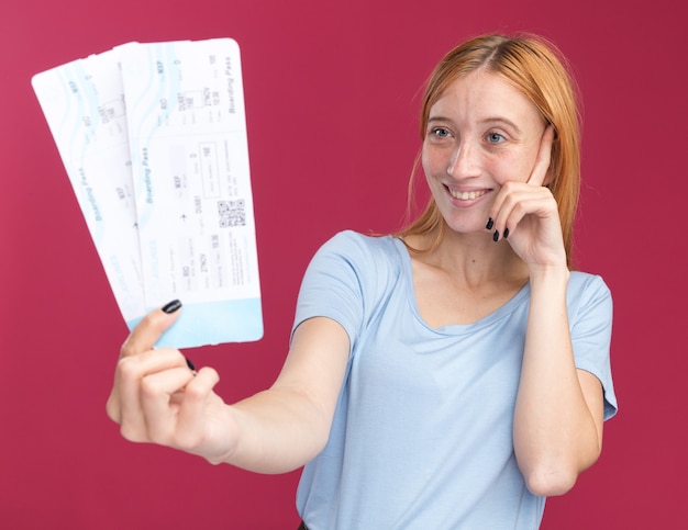 Free Photo pleased young redhead ginger girl with freckles puts finger on temple and holds air tickets isolated on pink wall with copy space