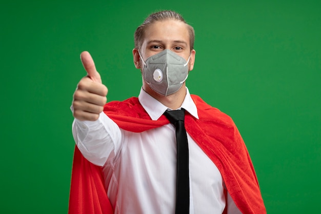 Free photo pleased young superhero guy wearing medical mask and tie showing thumb up isolated on green