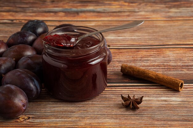 Plum confiture in a glass jar on a wooden board.