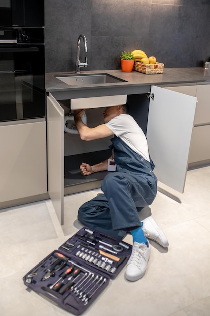 Free photo plumbing inspection man in overalls with badge reclining on floor with tools