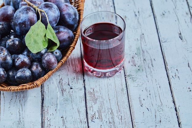 Free Photo plums in a basket on blue with a glass of juice.