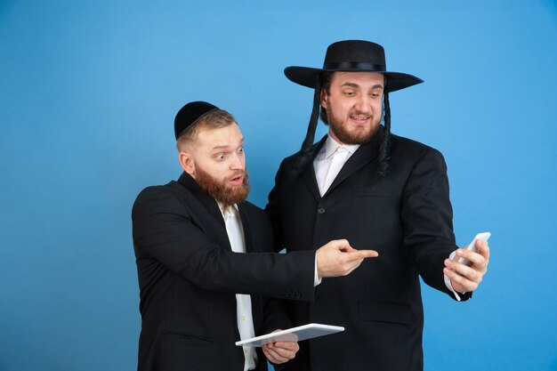 Pointing, choosing. Portrait of a young orthodox jewish men isolated on blue  wall. Purim, business, festival, holiday, celebration Pesach or Passover, judaism, religion concept.