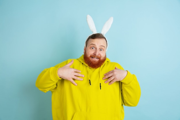 Free photo pointing on himself. caucasian man as an easter bunny with bright casual clothes on blue studio background.