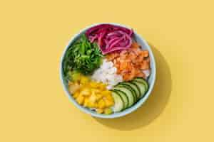 Free photo poke bowl with rice salmoncucumbermangoonionwakame salad poppy seeds ands sunflowers seeds isolated on yellow backgroundxa