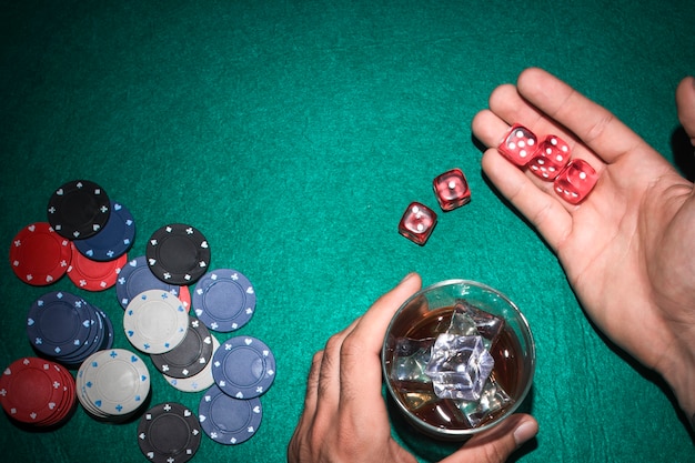 Free photo poker player showing red dices with glass of whiskey on poker table