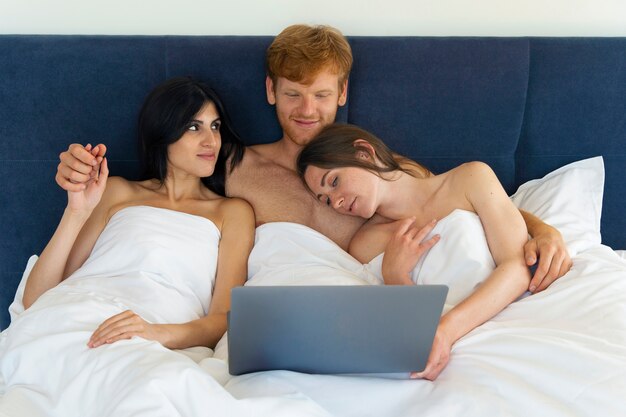 Polyamorous couple at home in bed with laptop