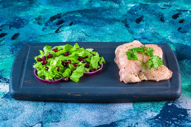 Free photo pomegranate arils, lettuce leaves with onion ring next to chicken breast on a wooden tray