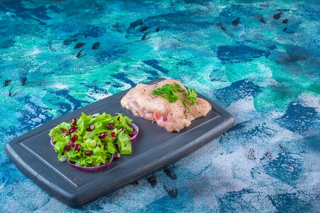 Free photo pomegranate arils, lettuce leaves with onion ring next to chicken breast on a wooden tray