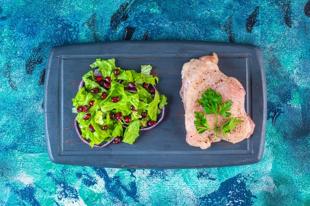 Pomegranate arils, lettuce leaves with onion ring next to chicken breast on a wooden tray 