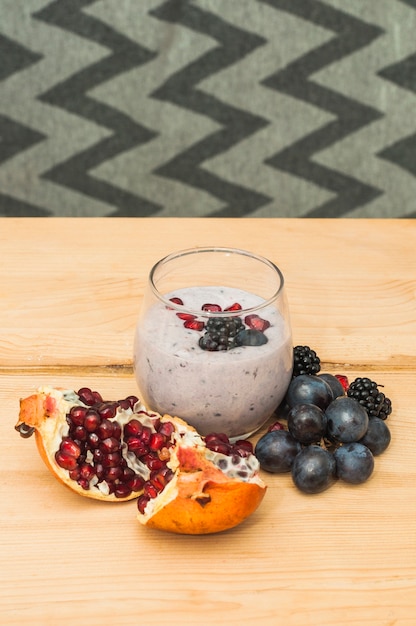 Pomegranate; grapes and raspberries smoothies on wooden table against wallpaper