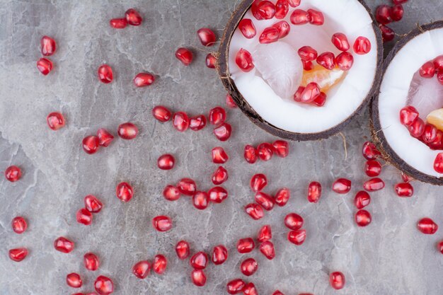 Pomegranate seeds inside coconuts and on surface. 