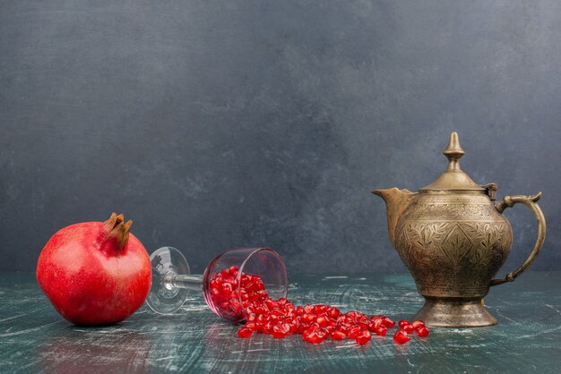 Free Photo pomegranate seeds scattered on marble table with teapot.