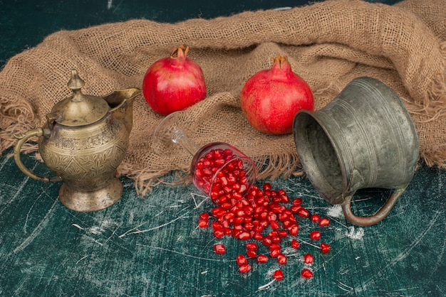 Free Photo pomegranate seeds scattered on marble table with vase and teapot.