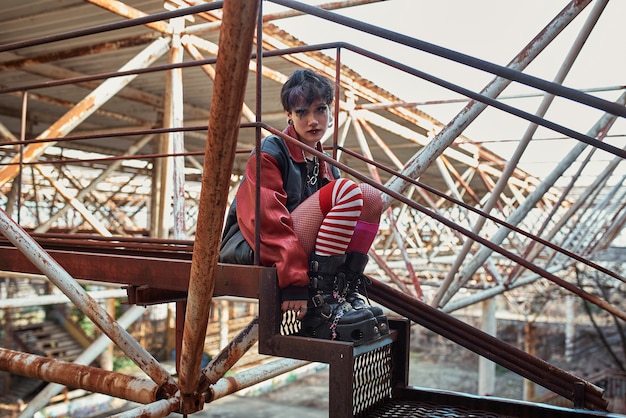 Pop punk aesthetic portrait of woman posing on metal structure on stairs