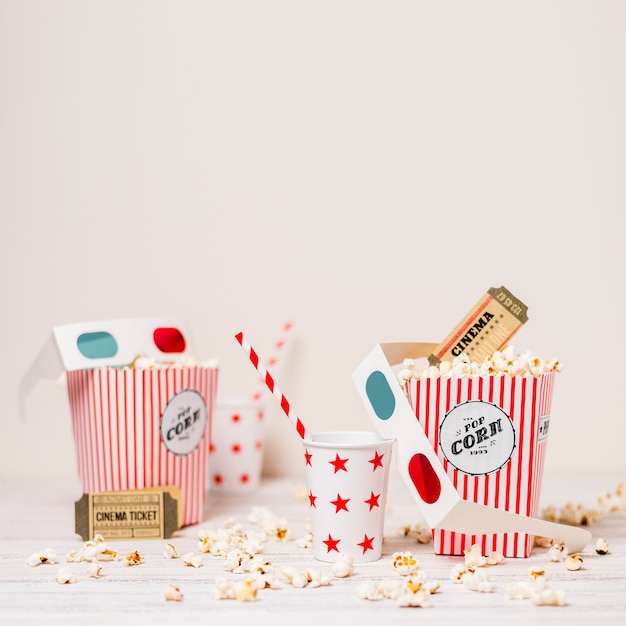 Popcorn; cinema ticket; disposable glass with drinking straw and popcorn box on table against white background