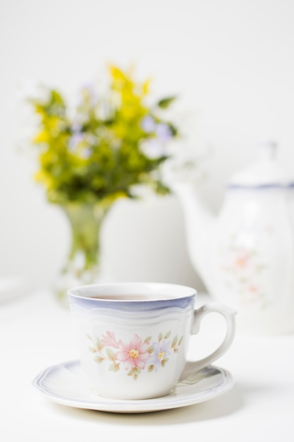 Porcelain cup of tea and saucer on white table against selective background