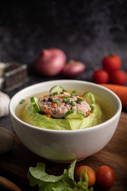 Pork cabbage soup with carrots, chopped green onions, cucumber in a wooden plate on a wooden plate