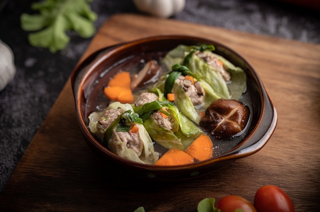 Pork cabbage soup with carrots, chopped green onions, cucumber in a wooden plate on a wooden plate