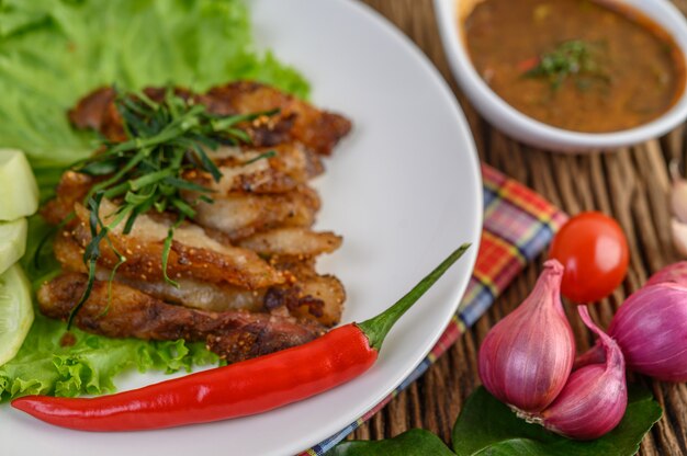 Pork neck grilled on a white plate wiht red onion, tomato, and chili on the wooden table.