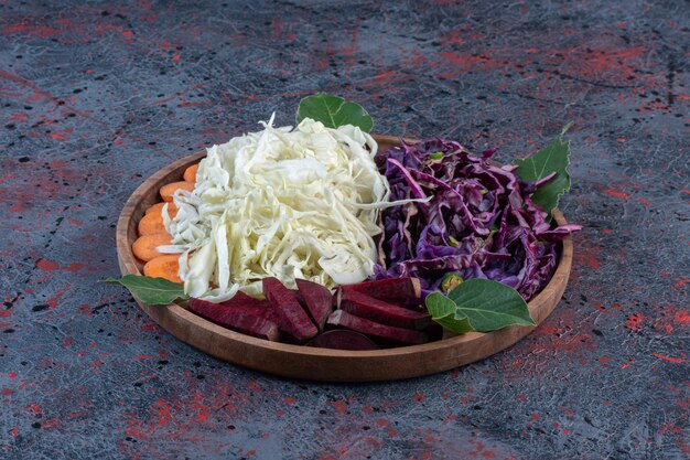 Portions of chopped red and white cabbages, beets and carrots on a tray on dark colored background. High quality photo