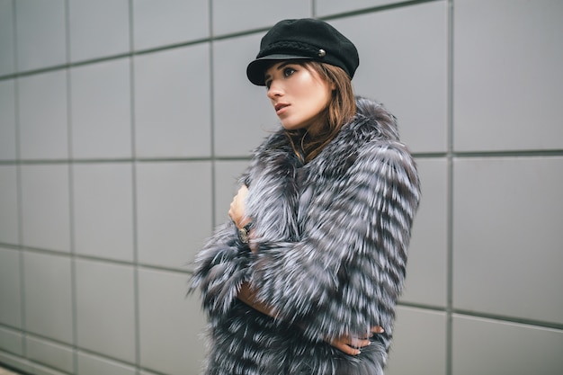 Free photo portrair of fashionable woman walking in city in warm fur coat, winter season, cold weather, wearing black cap, street fashion trend