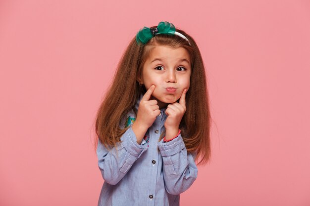 Portrait of adorable little girl with beautiful long auburn hair blowing up her cheeks touching face