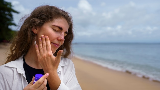 Portrait of adult woman applying lotion on sunburn skin