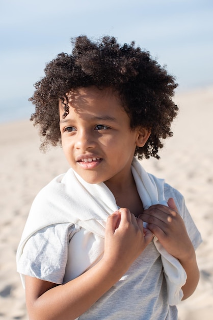 Free photo portrait of african american child on beach alone. female model with curly hair in t-shirt and sweatpants posing. portrait, beauty concept