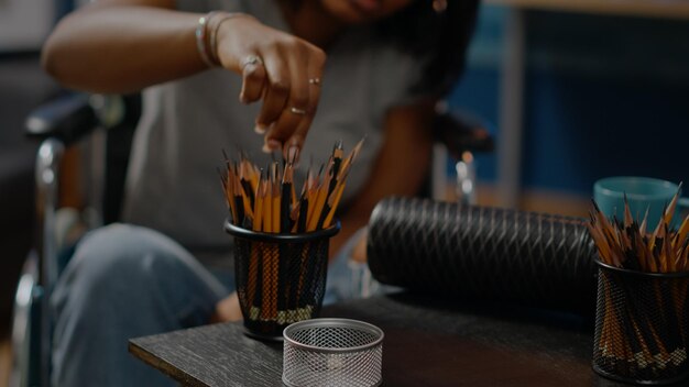 Portrait of african american woman drawing on canvas in workshop space. Close up of art pencils on table used by black young artist sitting in wheelchair creating masterpiece