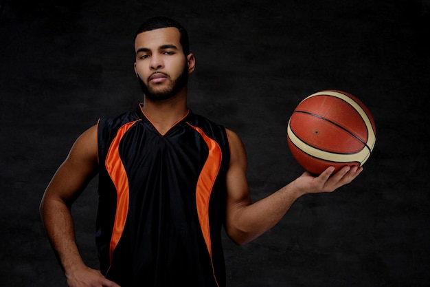 Free photo portrait of an afro-american sportsman. basketball player in sportswear with a ball on a dark background.