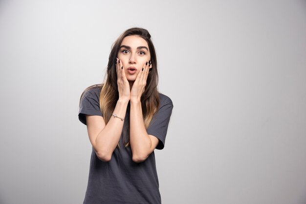 Portrait of amazed woman touching her face posing over gray background.